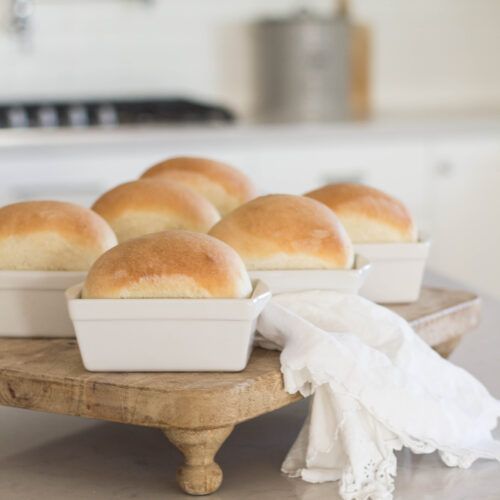 bread rolls sitting in white dishes on a wooden tray