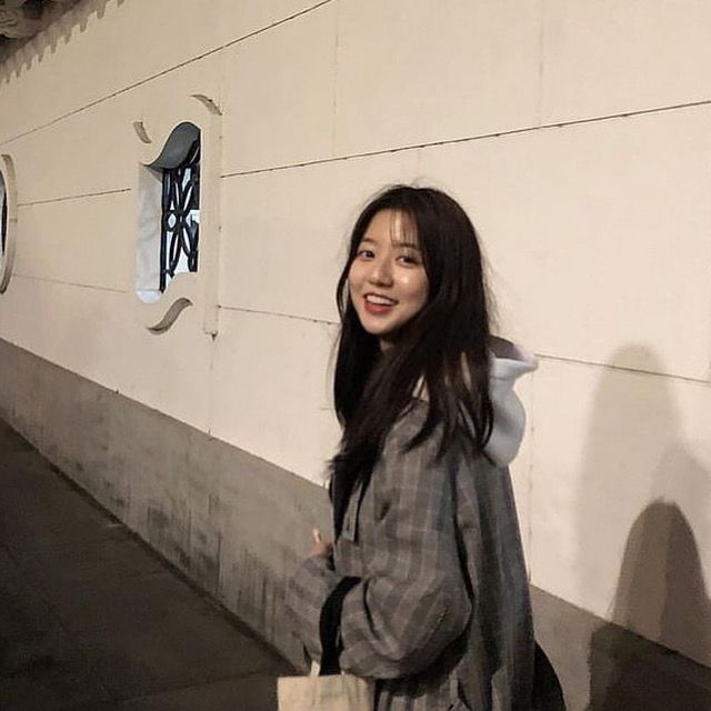 a woman standing in front of a wall holding a bag and looking at the camera