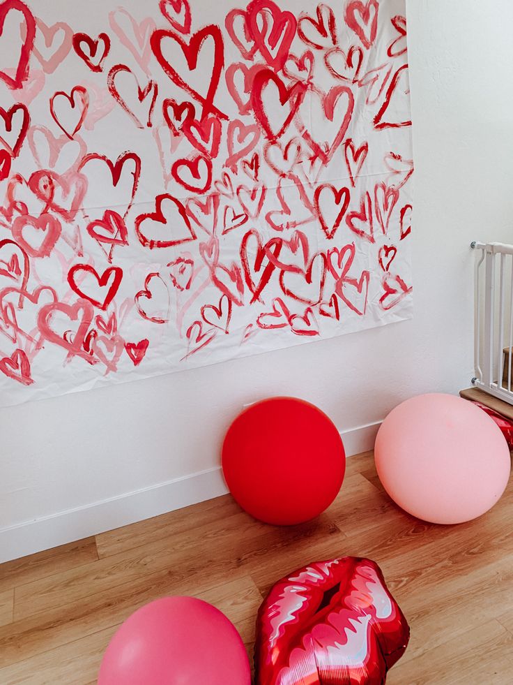 red and pink balloons on the floor in front of a wall with hearts drawn on it