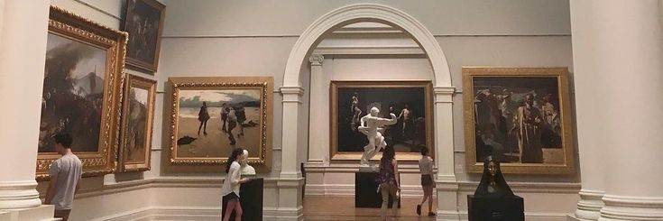 people looking at paintings on display in a museum gallery with columns and arches around them