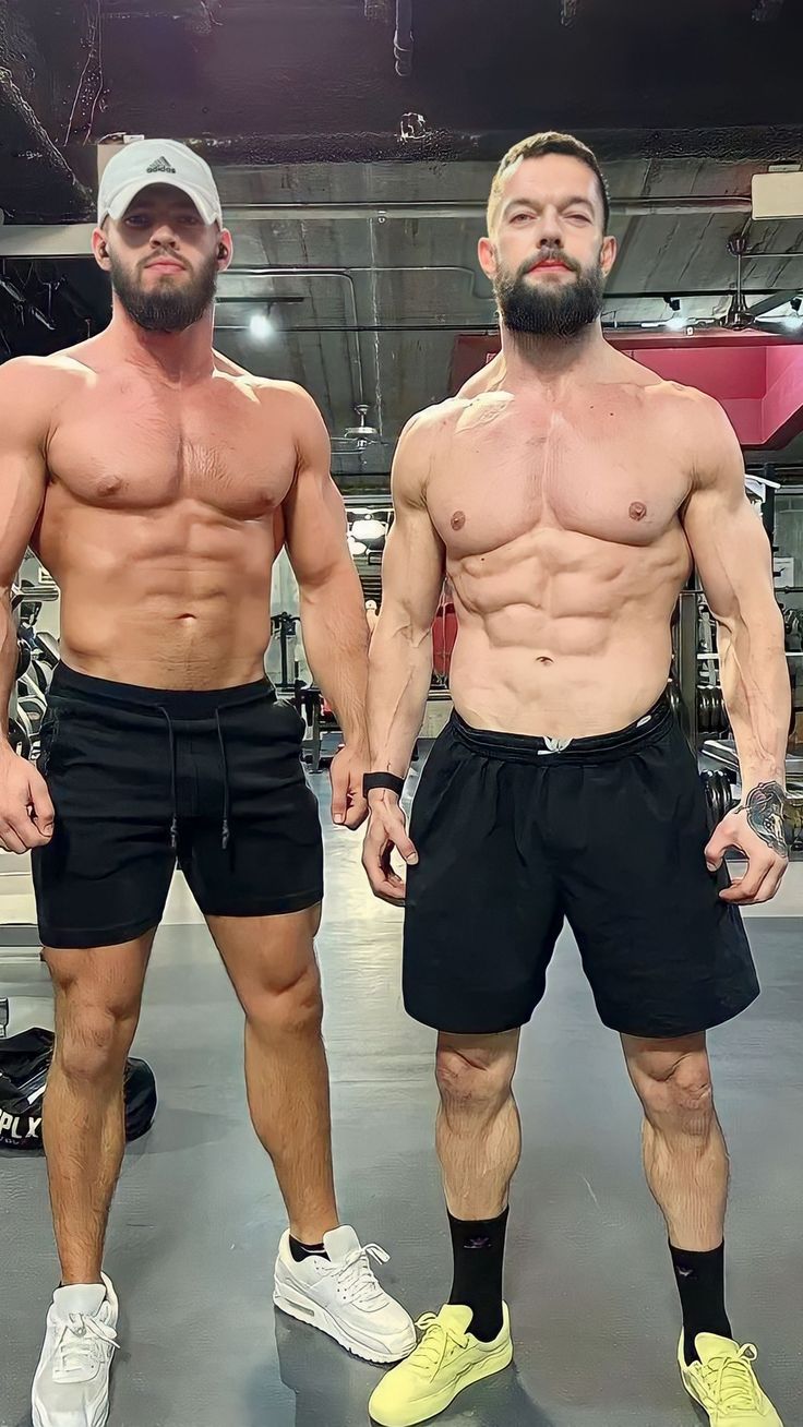 two men standing next to each other in the middle of a gym area with no shirts on