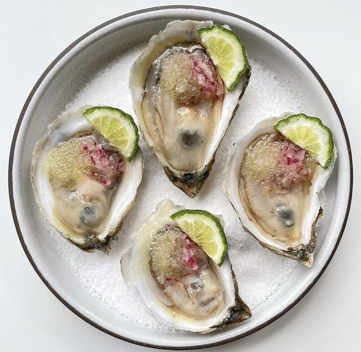 four oysters on a plate with lime wedges