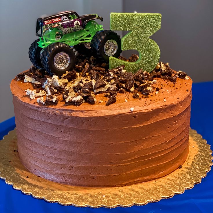 a birthday cake with a green monster truck on top and the number three spelled out