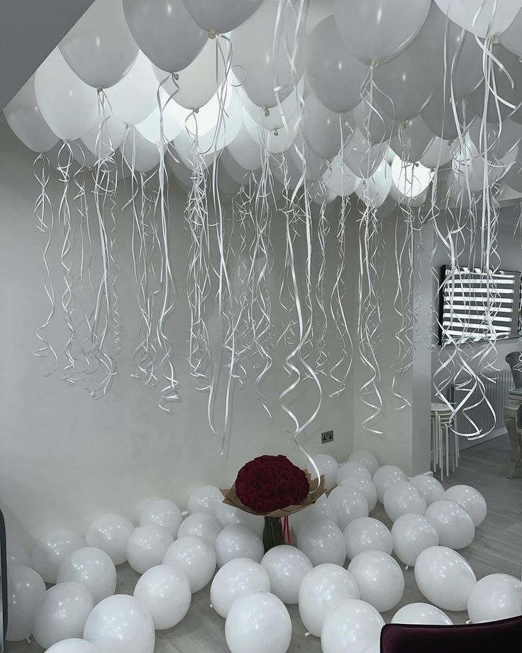 white balloons and streamers hang from the ceiling above a room with a red rose