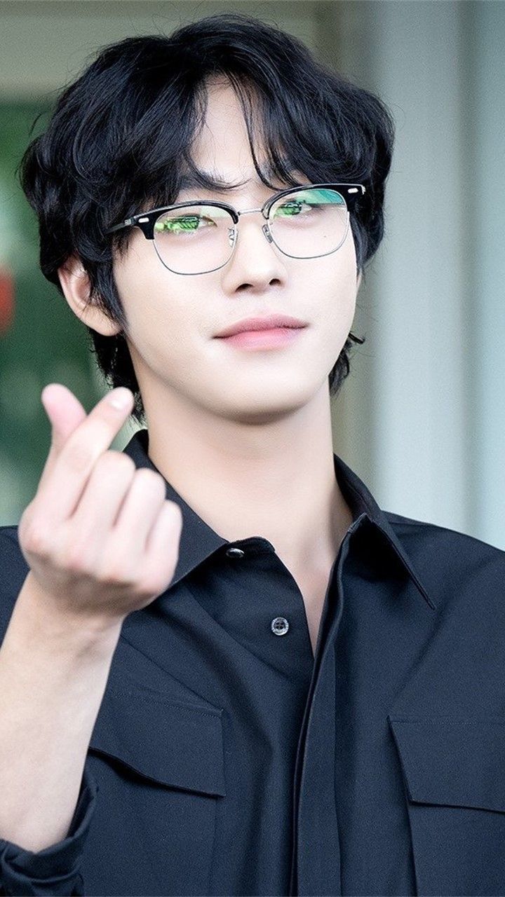 a young man wearing glasses making the middle finger sign with his hand while standing in front of a building