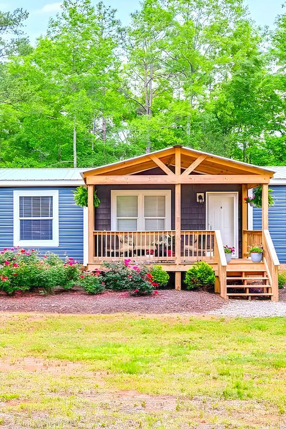 a mobile home sits in the middle of a wooded area with flowers and trees around it