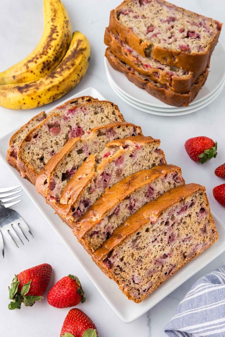 slices of strawberry banana bread on plates next to sliced strawberries and two forks with bananas in the background