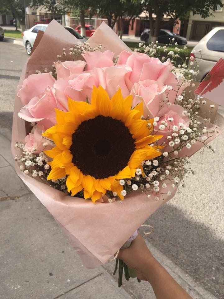 a bouquet of sunflowers and baby's breath is held by someone on the sidewalk