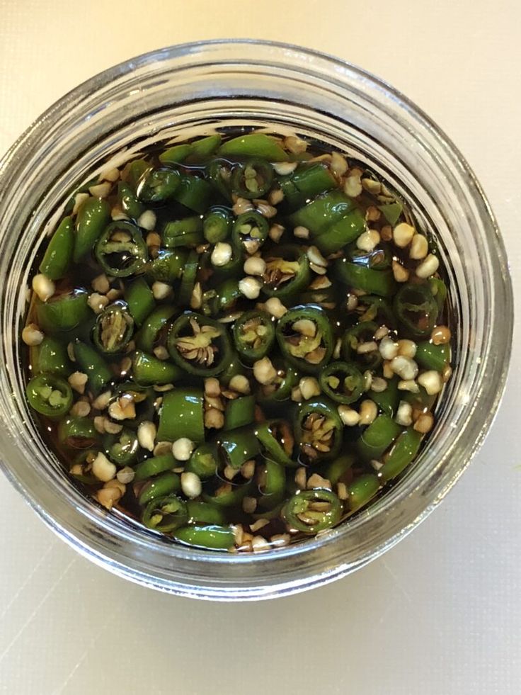 a glass jar filled with green peppers on top of a table