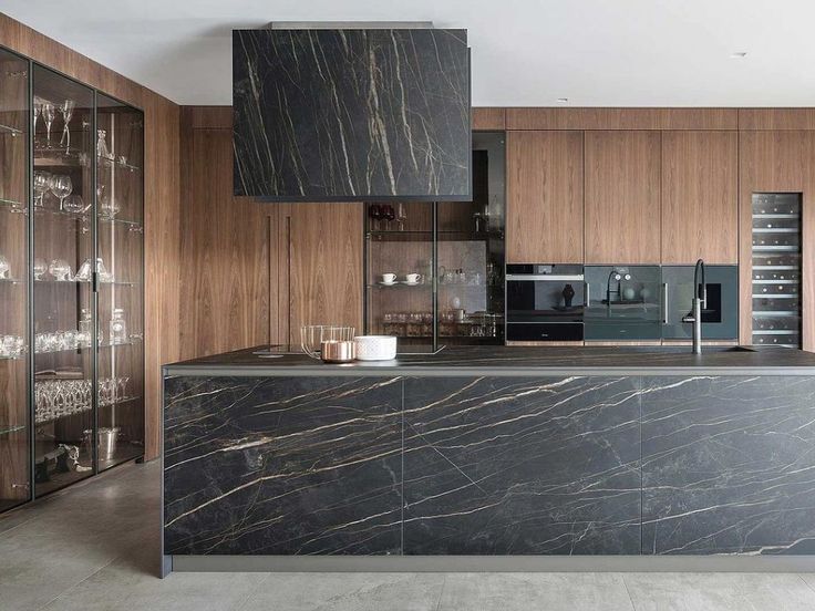 a modern kitchen with marble counter tops and wooden cabinets, along with wine glasses on the shelves