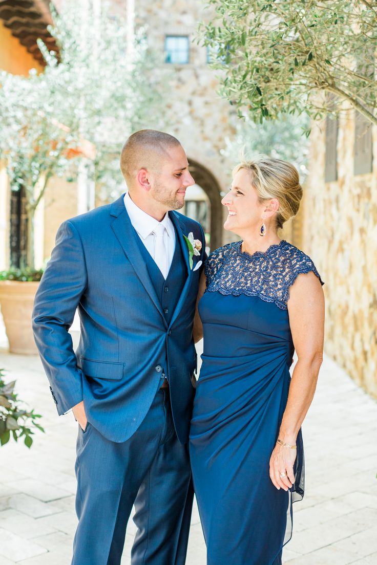 a man and woman standing next to each other in front of an olive tree wearing blue dresses