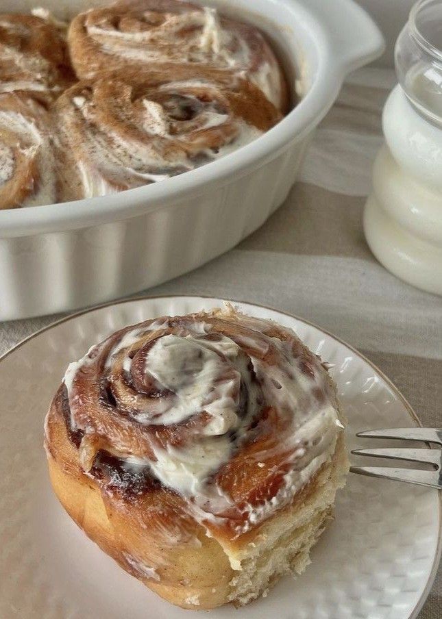 a plate with a pastry on it next to a bowl of cinnamon rolls