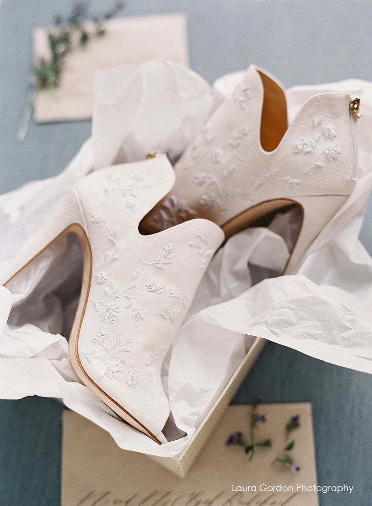 a pair of white high heels sitting in a box on top of a blue table