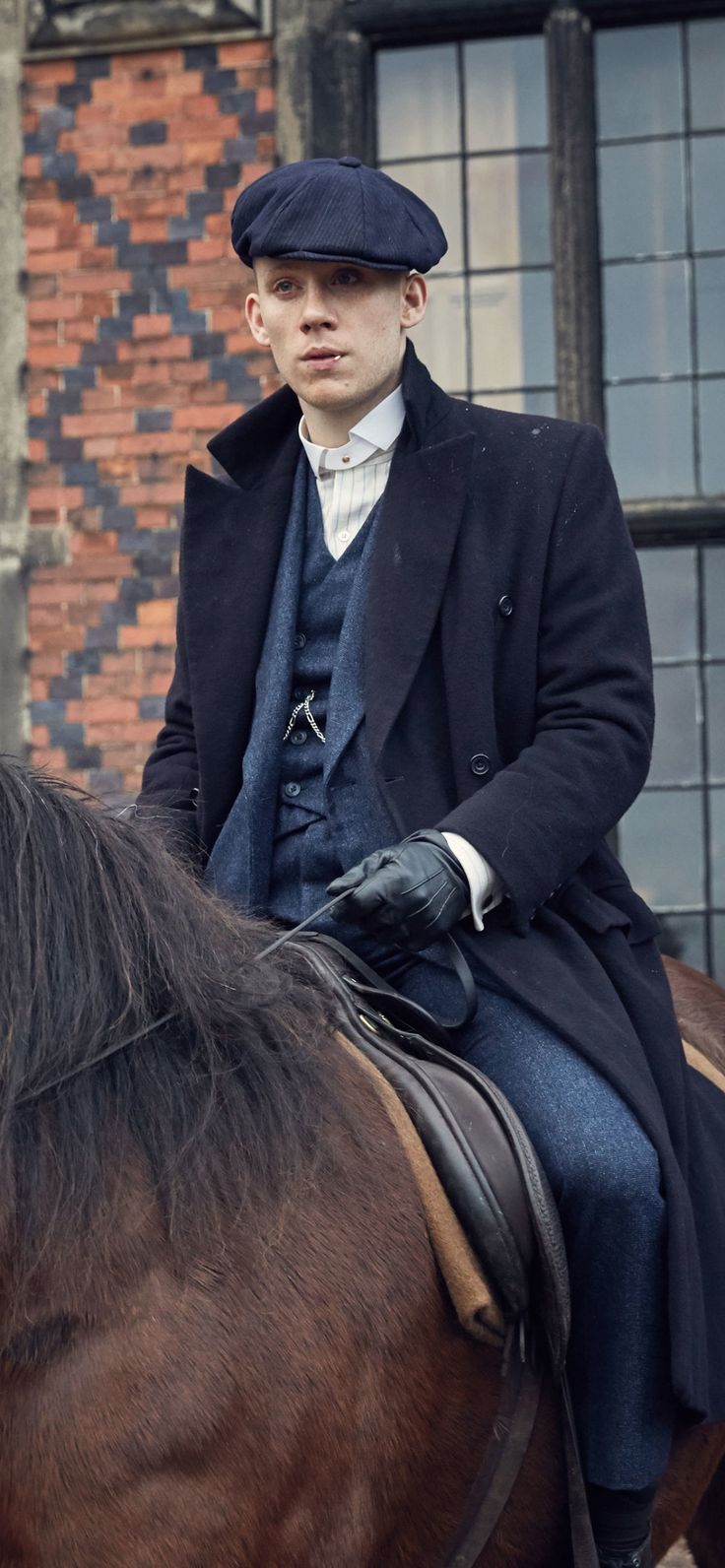 a man riding on the back of a brown horse next to a brick building with windows