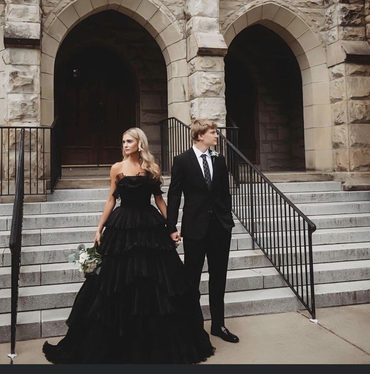 a man and woman dressed in formal wear walking down stairs together, with one holding the hand of the other's hand