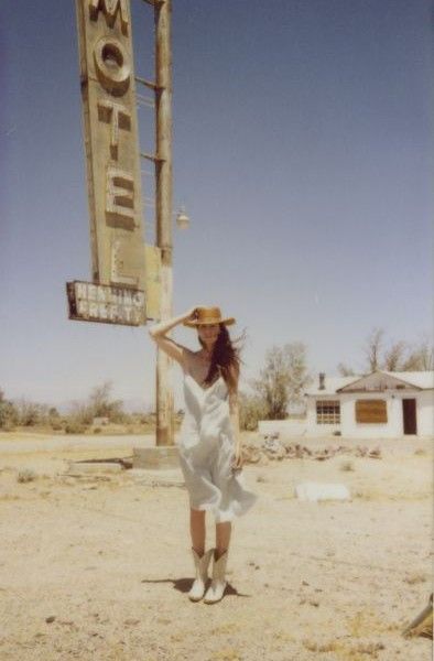 a woman in a white dress and hat standing next to a sign for a motel