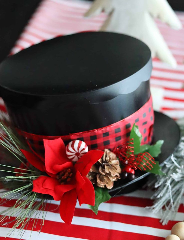 a black top hat with red and green decorations on it sitting on a striped table cloth