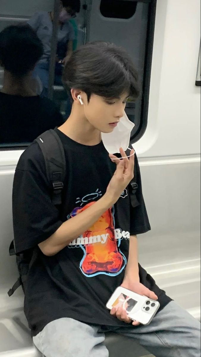 a young man sitting on the side of a train holding a cell phone