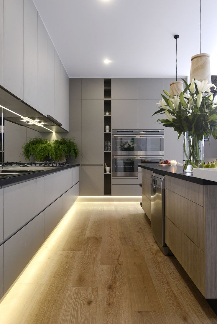 a modern kitchen with wooden floors and white cabinetry is lit by recessed lighting