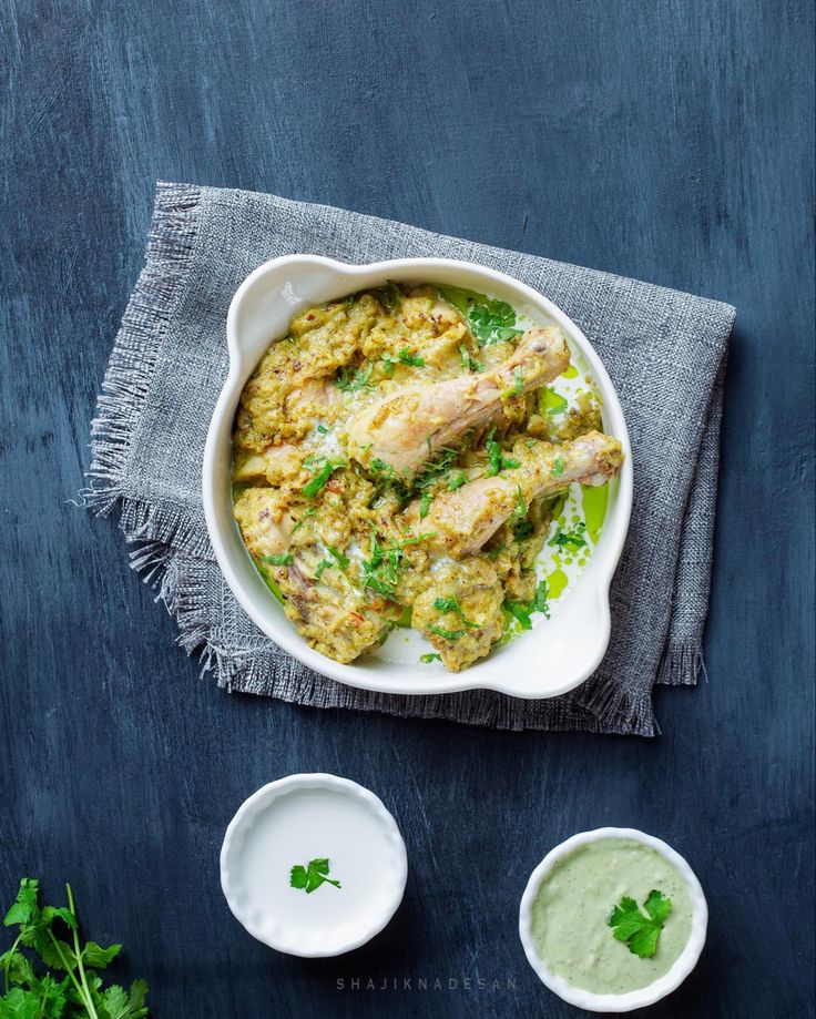 a white bowl filled with chicken and rice next to two small bowls of green sauce