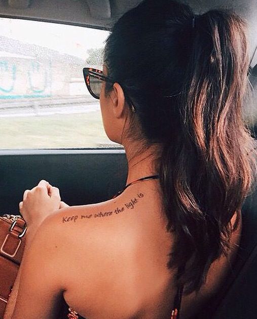 a woman sitting in the back seat of a car with tattoos on her upper arm