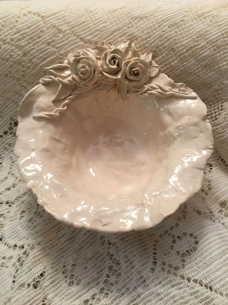 a white bowl sitting on top of a lace covered tablecloth with flowers in it