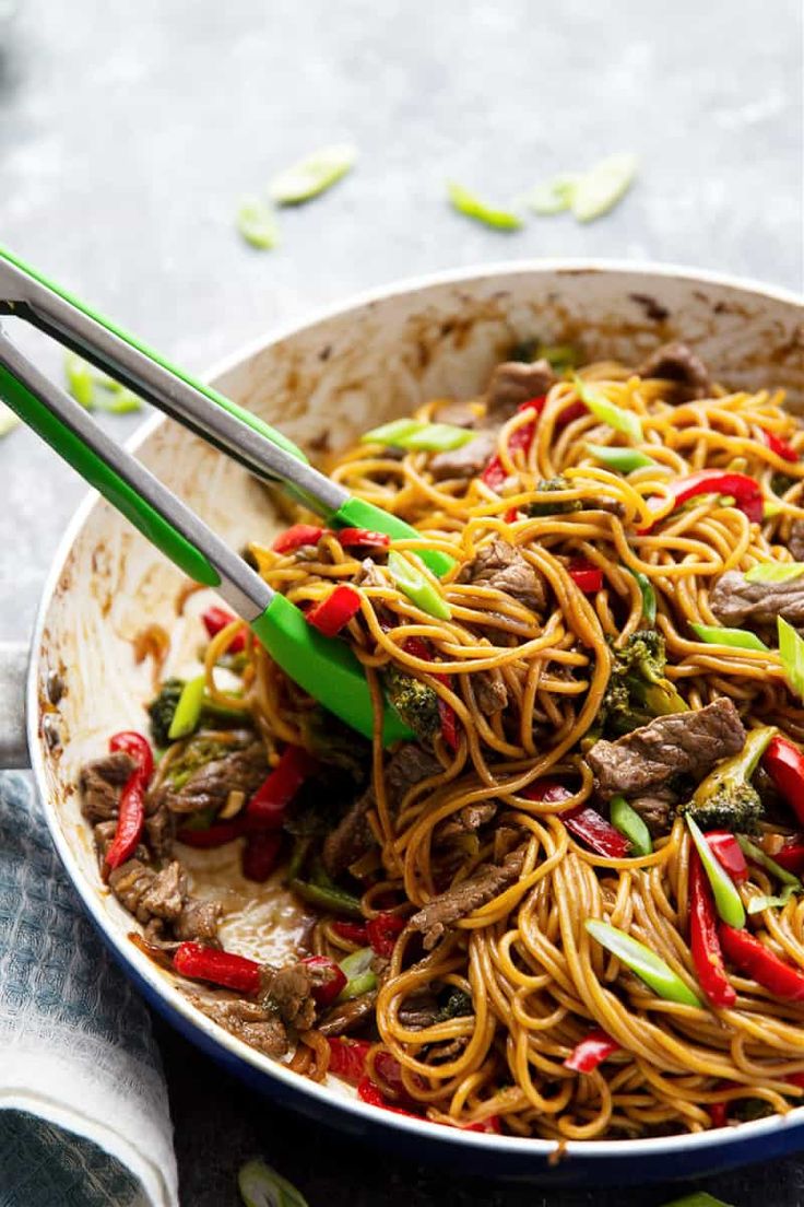 stir fry noodles with beef and vegetables in a pan on a table top, ready to be eaten