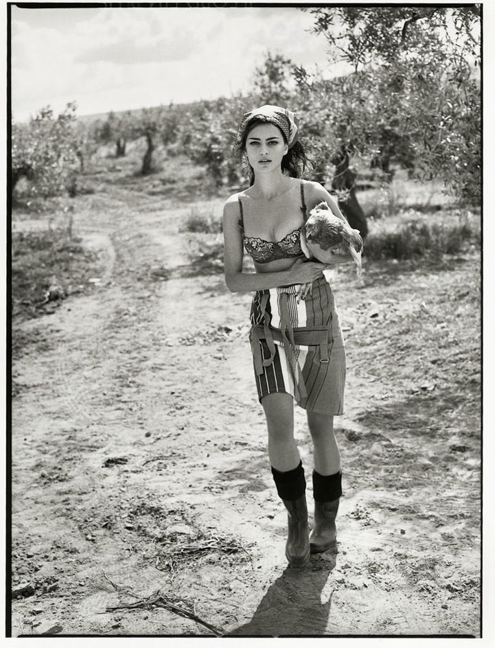 black and white photograph of a woman holding a teddy bear in the middle of a dirt road