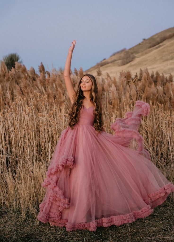 a girl in a pink dress standing in a field with her arms up and smiling at the camera