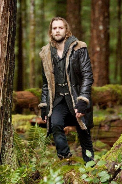 a man standing in the woods wearing a leather coat