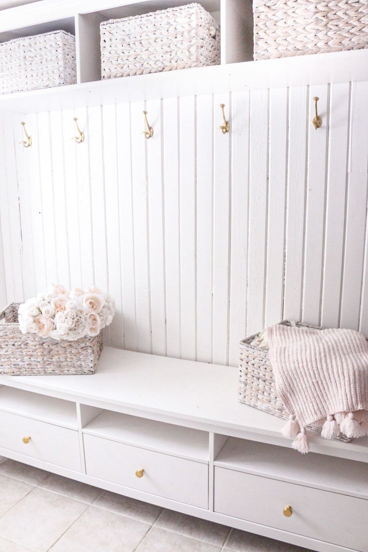 a white bench with baskets and flowers on it next to a wall mounted coat rack