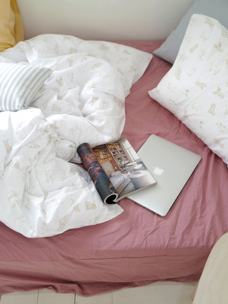 an open laptop computer sitting on top of a bed next to pillows and blankets,