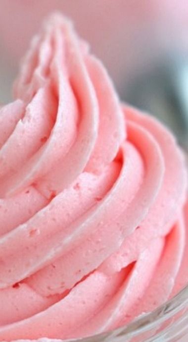 a close up of a pink frosted cupcake in a glass bowl on a table