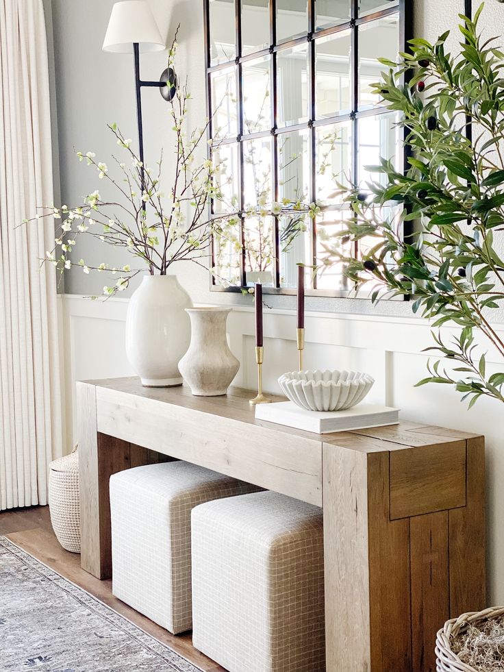 a white vase sitting on top of a wooden table next to a mirror and plant