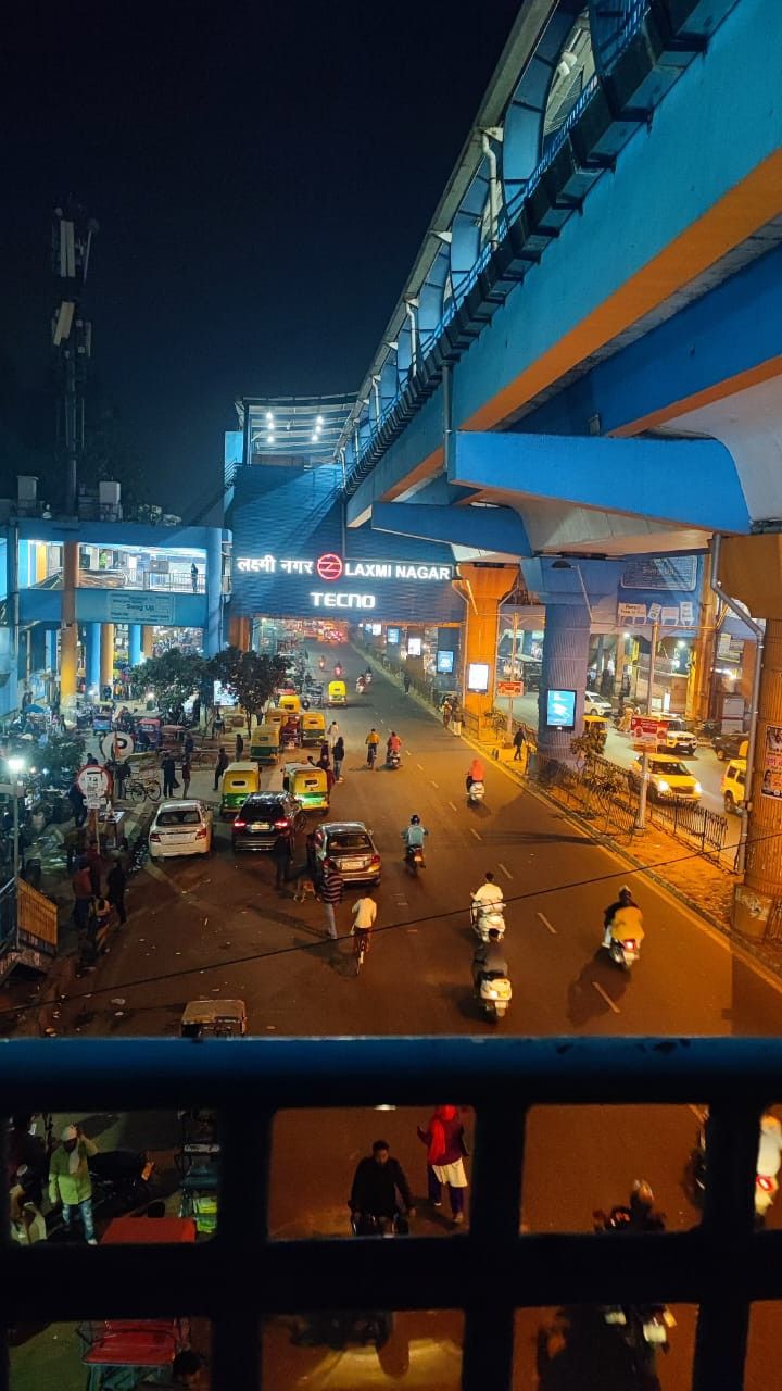 people are walking down the street at night in an urban area with cars and motorcycles