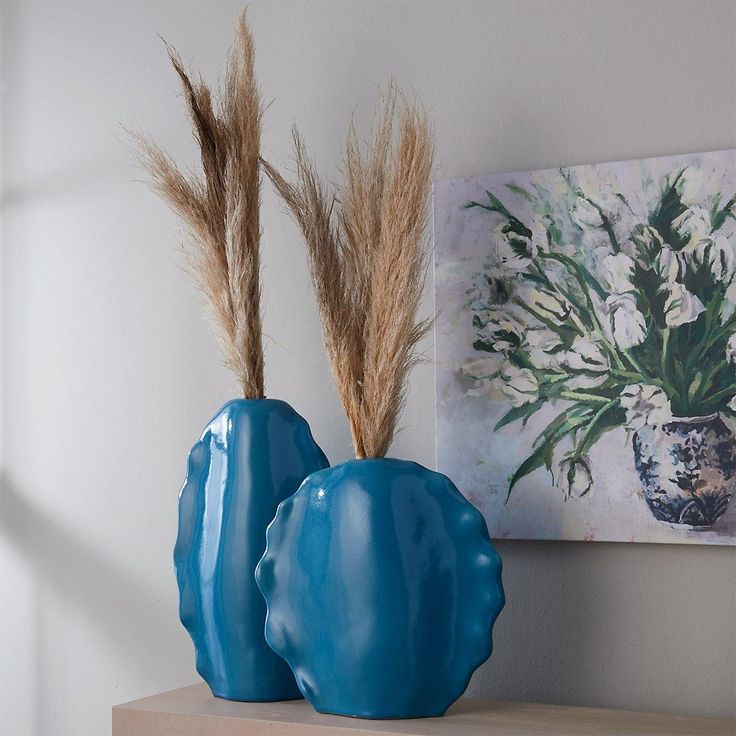 two blue vases sitting on top of a wooden shelf next to a painting and flowers