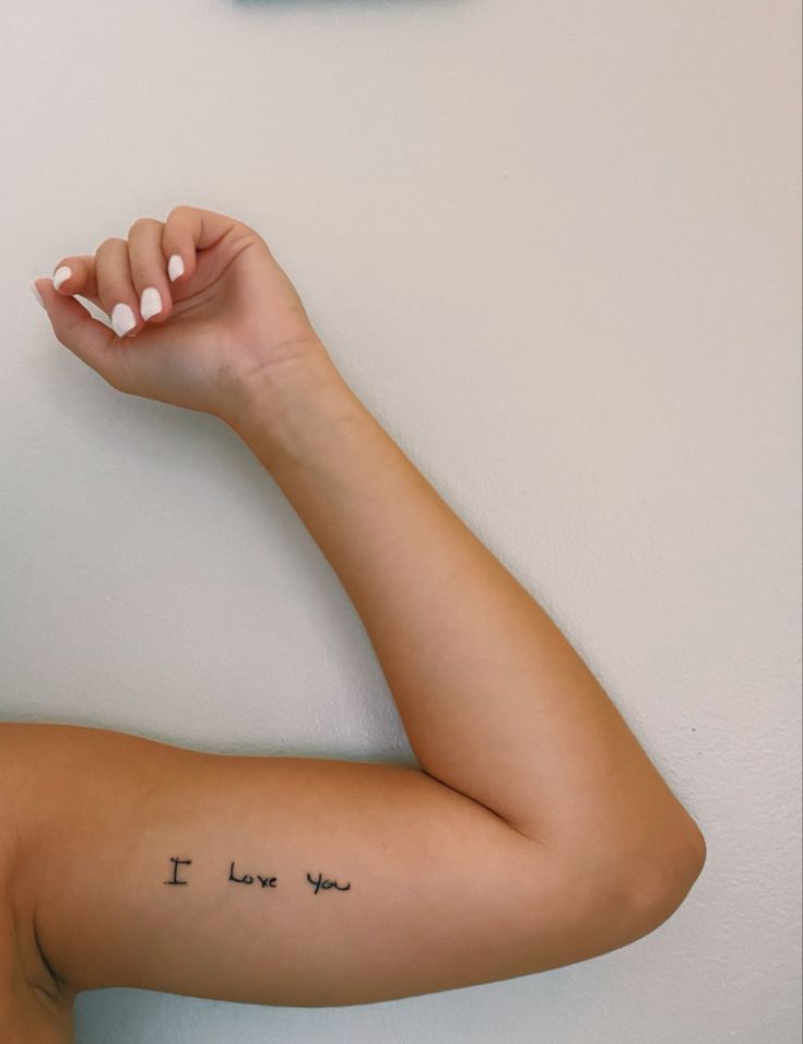 a woman's arm with the words i love you written on it and a clock behind her