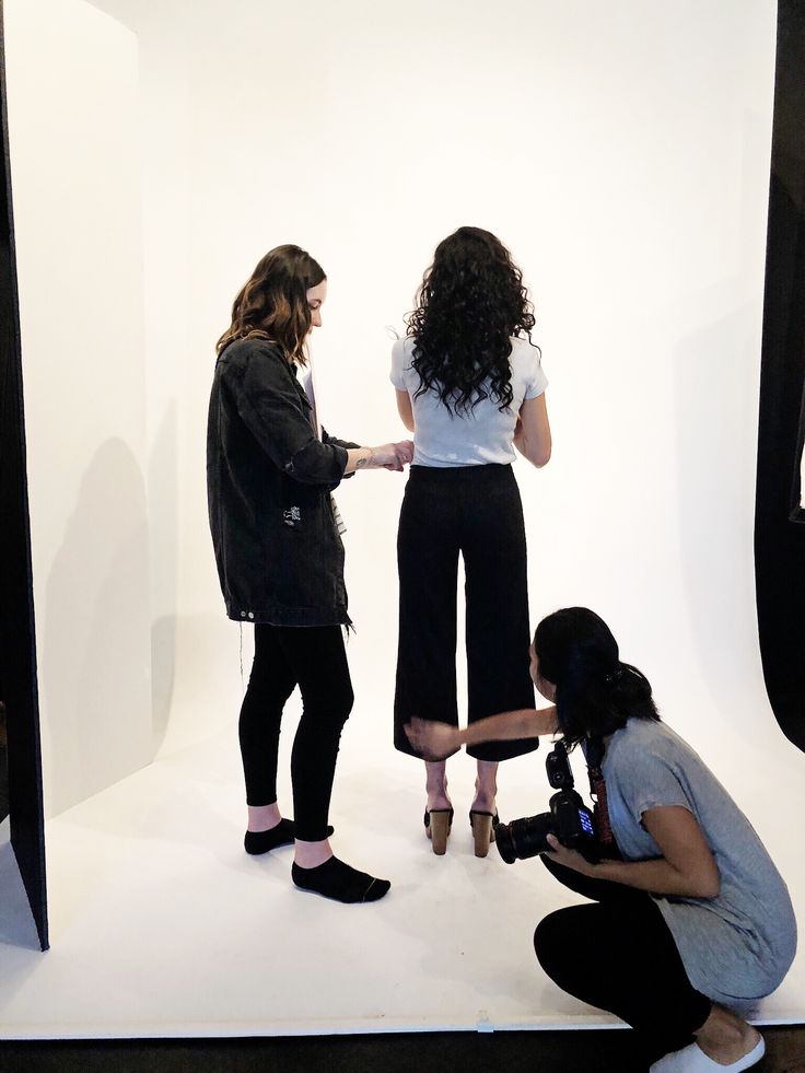 three women are standing in front of a white backdrop and one is holding a camera