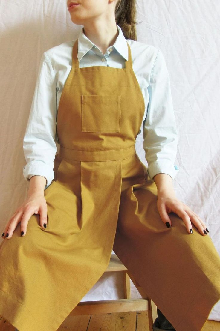 a woman sitting on top of a wooden chair wearing overalls and holding her hands in her pockets