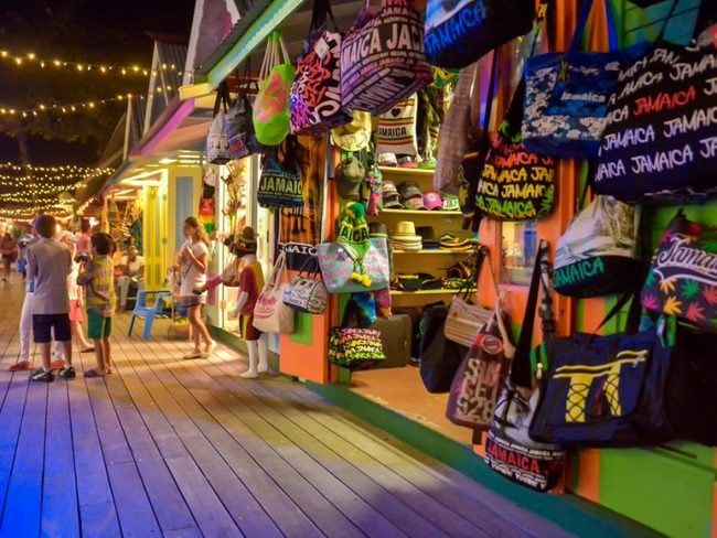 many people are shopping at an outdoor market with lights strung over the storefronts