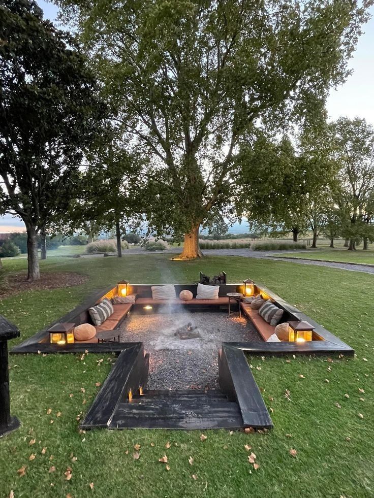 a fire pit in the middle of a grassy area with couches and candles on it