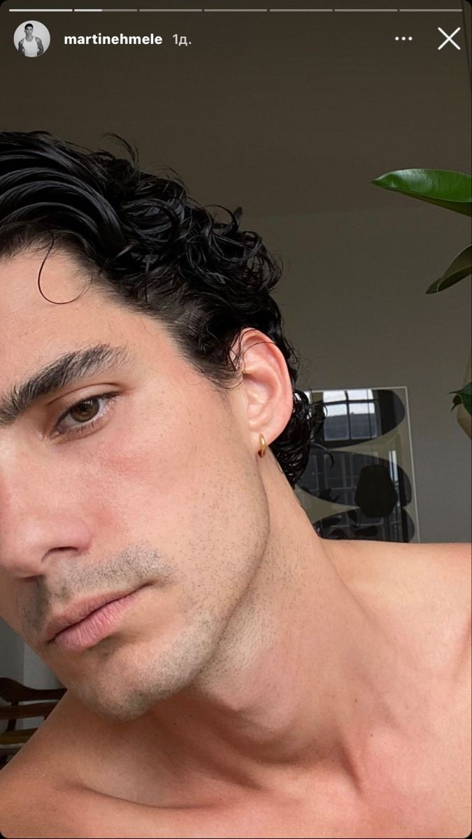 a man with curly hair and no shirt is looking at the camera while wearing earrings