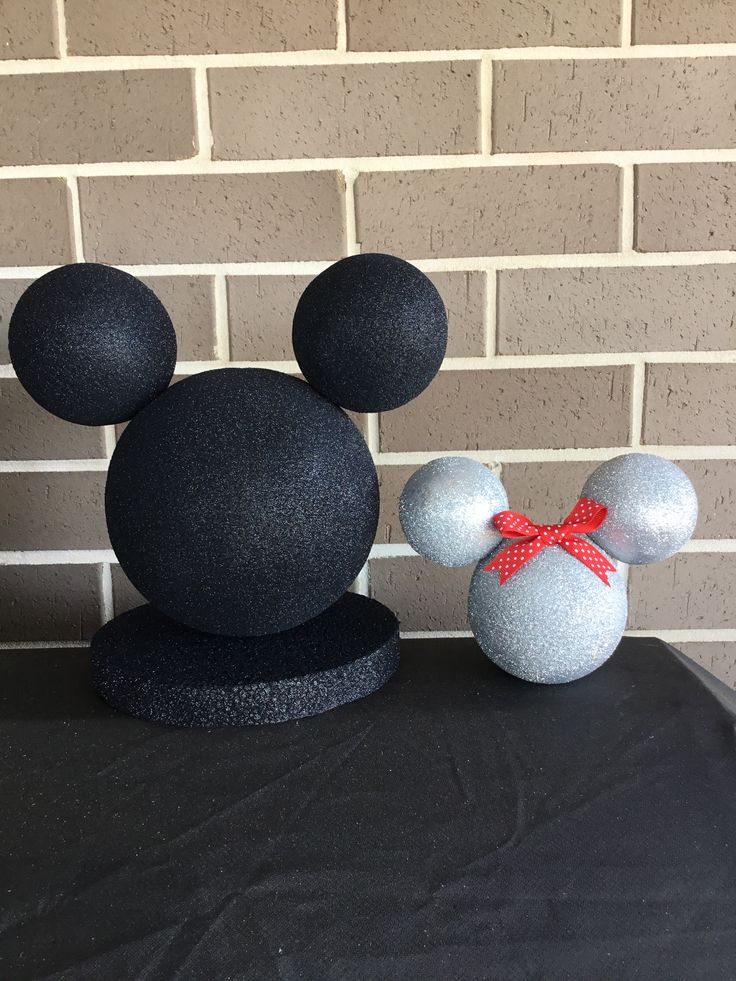 two mickey mouse heads sitting on top of a black table next to a brick wall