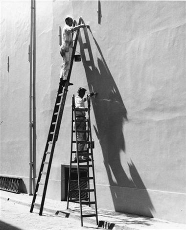 two men are painting the side of a large white building while another man is standing on a ladder