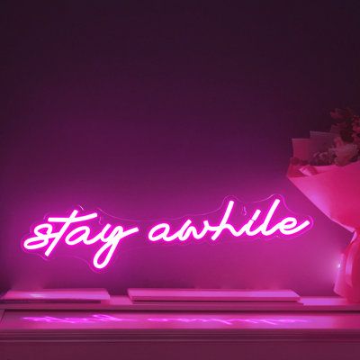 a neon sign that says stay awhile in front of a vase with flowers on it