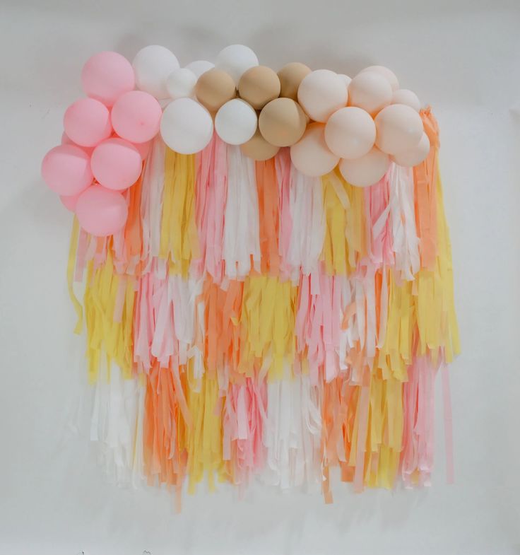 balloons and streamers are arranged on a white tablecloth with pastel orange, pink, yellow, and beige colors