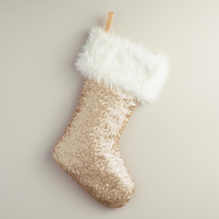 a gold christmas stocking with white fur hanging from a wooden stick on a gray background