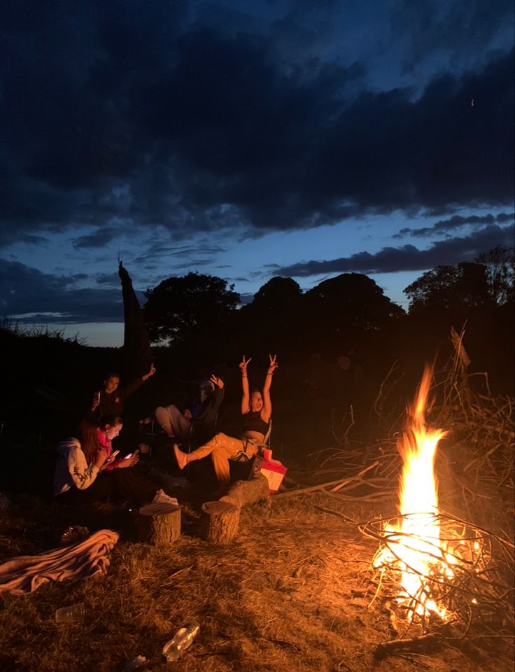 people sitting around a campfire with their arms in the air and one person reaching up