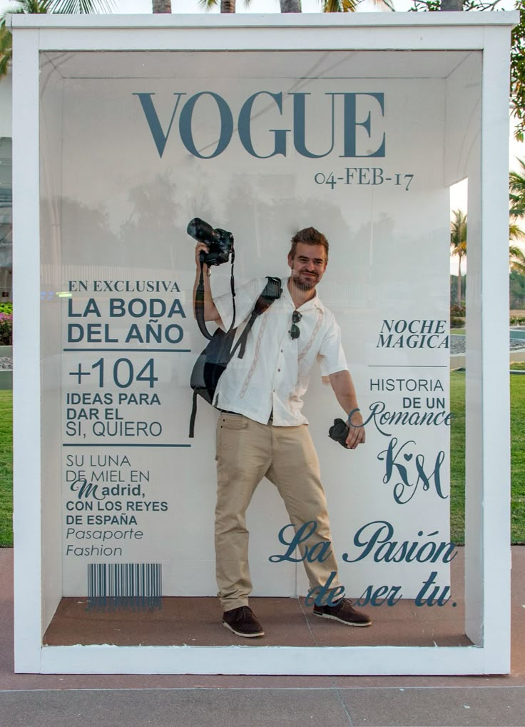 a man standing in front of a sign with his hands on his hips and holding a camera