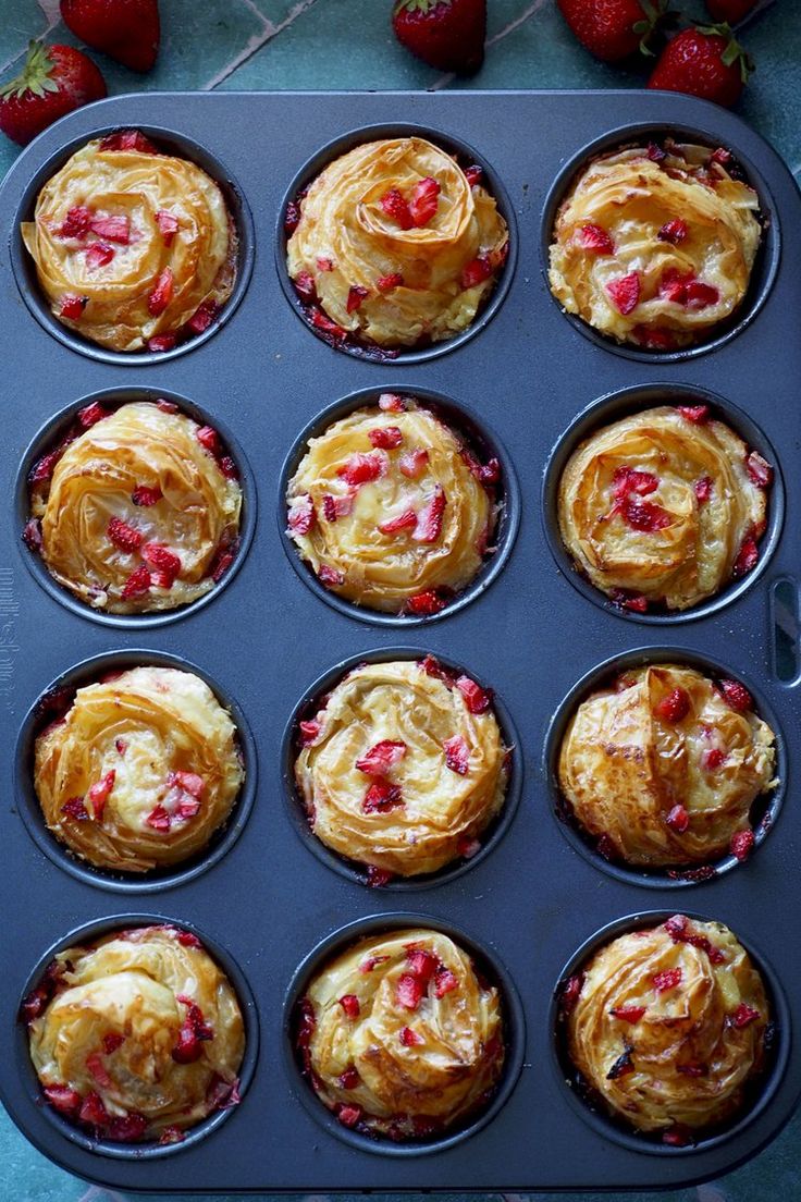 someone holding a muffin in a pan with strawberries on the side